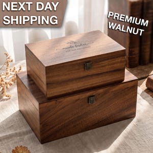 May include: Two rectangular walnut wood boxes with hinged lids and metal latches. The top box features an engraved floral design with the text "NICOLE FISHER" and "FOR LOVE AND MEMORY". The wood grain is visible on the dark brown surfaces.