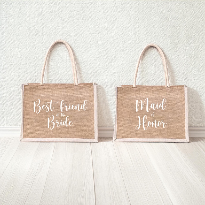 Pode incluir: Duas sacolas de juta com al&ccedil;as brancas e texto branco. A sacola &agrave; esquerda diz "Melhor amiga da noiva". A sacola &agrave; direita diz "Madrinha de honra".