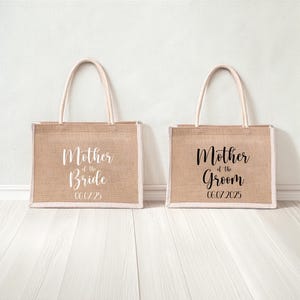 Pode incluir: Duas sacolas de juta com al&ccedil;as brancas. A sacola &agrave; esquerda diz "M&atilde;e da Noiva" com a data "06/07/25". A sacola &agrave; direita diz "M&atilde;e do Noivo" com a data "06/07/2025".