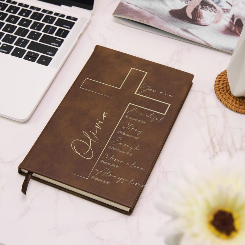 Puede incluir: Un diario de cuero marr&oacute;n con un dise&ntilde;o de cruz y el nombre "Olivia" en letras doradas. El diario incluye texto inspirador: "Beautiful, Strong, Enough, Never alone, Always loved."