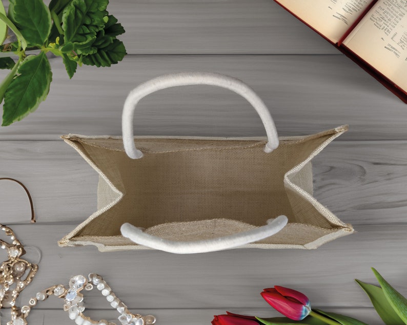 Pode incluir: Uma bolsa tote de juta bege com al&ccedil;as brancas. A bolsa est&aacute; vazia e aberta, mostrando o interior da bolsa.