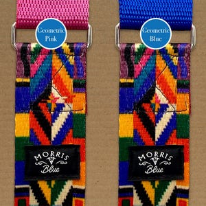 May include: Two guitar straps with a colourful geometric pattern. The strap on the left is pink and the strap on the right is blue. Both straps have a black label that says "Morris Blue".