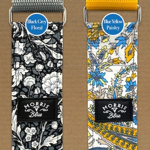 May include: Two guitar straps with different patterns. The strap on the left is black and grey with a floral pattern and the text "Black Grey Floral". The strap on the right is white with a blue and yellow paisley pattern and the text "Blue Yellow Paisley". Both straps have a black label with the text "Morris Blue".