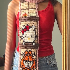 May include: A brown and beige crocheted scarf with a pink trim. The scarf features a Hello Kitty and a cartoon tiger.