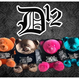 Könnte beinhalten: Vier Plüschteddys in Orange, Bronze, Pink und Türkis. Jeder Bär trägt einen schwarzen Kapuzenpullover mit weißen Buchstaben und einem Etikett. Der Hintergrund ist ein dunkelgraues Muster mit dem Text "D12" in Weiß.