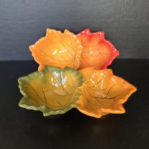 May include: A ceramic leaf-shaped serving dish with three sections. The dish features a gradient of colors, including orange, yellow, and green, with darker vein details. The dish is designed to resemble autumn leaves.