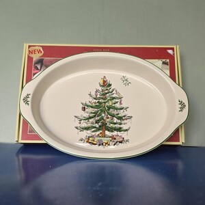 May include: Oval serving platter with a Christmas tree design. The off-white platter has a green trim and handles. The Christmas tree is decorated with ornaments and presents. The box behind the platter has the word "NEW" on it.