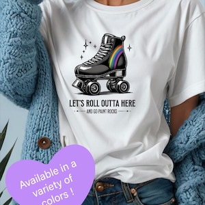 May include: White t-shirt featuring a black roller skate with a rainbow accent and the text "LET'S ROLL OUTTA HERE AND GO PAINT ROCKS." The image also includes a purple heart with the text "Available in a variety of colors!"