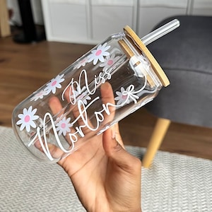 Pode incluir: Copo de vidro transparente com tampa e canudo de bambu. O copo &eacute; decorado com flores de margarida brancas e o nome "Miss Norton" em escrita branca. Projetado para bebidas frias.
