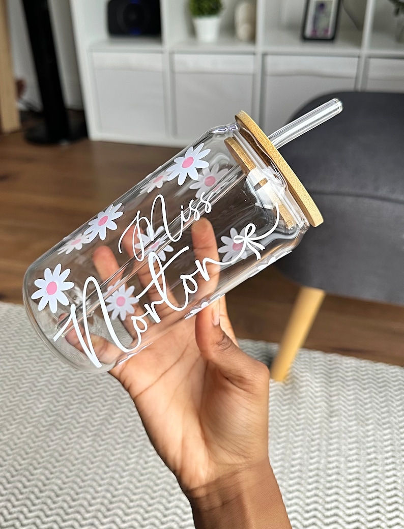Pode incluir: Copo de vidro transparente com tampa e canudo de bambu. O copo &eacute; decorado com flores de margarida brancas e o nome "Miss Norton" em escrita branca. Projetado para bebidas frias.