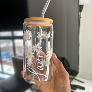 Pode incluir: Um copo de vidro transparente com tampa de bambu e canudo de vidro. O copo &eacute; decorado com margaridas brancas e o nome "Lauren" em escrita branca. O copo &eacute; segurado em uma m&atilde;o.