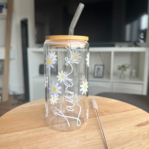 Pode incluir: Um copo de vidro transparente com tampa de bambu e canudo de vidro transparente. O copo &eacute; decorado com margaridas brancas e o nome "Lauren" em escrita branca. Um limpador de canudos de a&ccedil;o inoxid&aacute;vel est&aacute; ao lado do copo.
