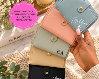 May include: A stack of five rectangular PU leather wallets in light blue, peach, sage green, beige, and black. Each wallet features a gold-tone snap button closure. The wallets are personalized with white or black text including names like Madeline, initials like EA, and the name Eky.