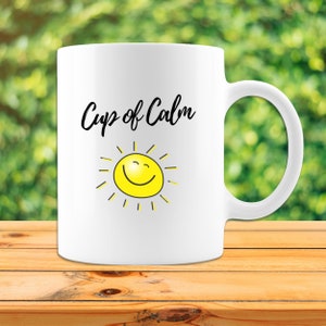 May include: White ceramic mug with a black and yellow design. The mug has the text "Cup of Calm" and a smiling sun with yellow rays.