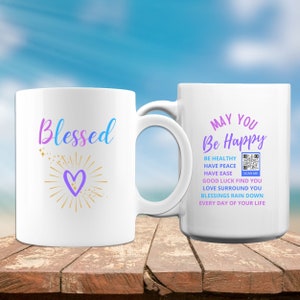May include: Two white coffee mugs with a design on each. The mug on the left has the word "Blessed" in rainbow colors with a gold heart and stars. The mug on the right has the text "May You Be Happy" in rainbow colors with a list of positive affirmations and a QR code.
