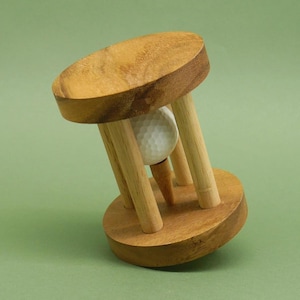 Könnte beinhalten: Ein hölzerner Golfballhalter mit einem Golfball und einem Tee im Inneren. Der Halter ist aus hellbraunem Holz gefertigt und hat eine runde Basis.