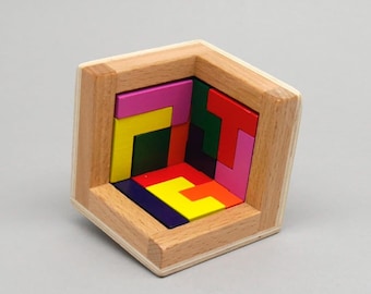 Könnte beinhalten: Eine Holzkiste mit einem bunten geometrischen Puzzle darin. Die Puzzleteile sind aus Holz und in verschiedenen Farben bemalt, darunter Rot, Gelb, Grün, Blau und Pink.