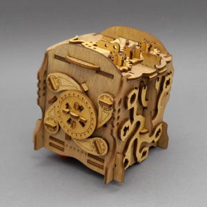 Könnte beinhalten: Eine mechanische Puzzle-Box aus hellbraunem Holz mit komplizierten lasergeschnittenen Details, darunter ein kreisförmiges Zifferblatt an der Seite, verschiedene ineinandergreifende zahnradartige Komponenten und komplexe Labyrinth-Muster.