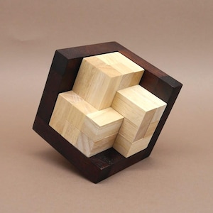 Könnte beinhalten: Ein Holzpuzzle mit ineinandergreifenden hellen Blöcken in einem dunkelbraunen Rahmen. Das Puzzle in Würfelform hat teilweise zusammengesetzte Blöcke. Die Holzmaserung ist auf den Blöcken und dem Rahmen sichtbar und erzeugt eine natürliche Ästhetik.