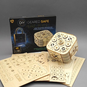 Puede incluir: Un kit de caja fuerte de engranajes de madera DIY. La caja dice "DIY GEARED SAFE" y "OPEN THE SECRET TREASURE BOX 10,000 possible password combinations". El kit incluye una caja, engranajes y láminas de madera con piezas recortadas.