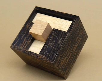 Può includere: Una scatola di puzzle in legno con una finitura marrone scuro e un blocco di legno marrone chiaro all'interno. La scatola è realizzata in legno con una venatura.