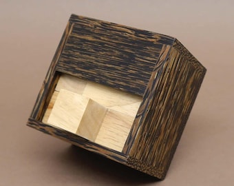 Può includere: Una scatola di puzzle in legno con un esterno in legno marrone scuro e un interno in legno chiaro. La scatola è aperta, rivelando i pezzi del puzzle all'interno.