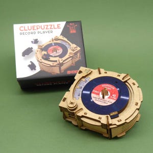 Könnte beinhalten: Ein 3D-Puzzle aus Holz, das einen Vintage-Plattenspieler darstellt. Das Puzzle ist zusammengebaut und zeigt eine blaue Schallplatte mit dem Text "Adventure Music" und "Song of Puzzles (45) Adventure Band".