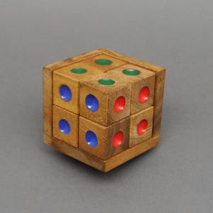 Peut inclure: Un cube de puzzle en bois avec un design cube-dans-un-cube. Le cube extérieur est en bois brun clair, avec des cercles colorés verts, bleus et rouges. Le puzzle est conçu pour être démonté et remonté.