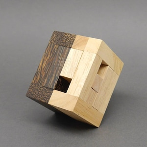Op de afbeelding: Een houten puzzelkubus gemaakt van licht en donker hout. De kubus is gemaakt van kleinere stukken die in elkaar passen om een ​​grotere kubus te vormen.