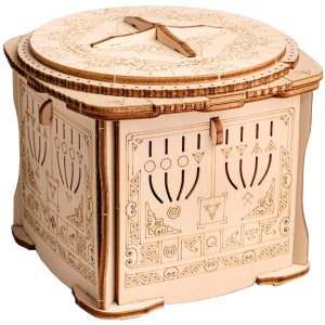 Könnte beinhalten: Eine Holz-Puzzlebox mit aufwendigen, lasergeschnittenen Designs. Die Box hat eine kreisförmige Oberseite mit einem kompassartigen Design und einen Klappdeckel. Die Seiten sind mit geometrischen Mustern und ausgeschnittenen Formen verziert. Die Box ist aus hellem Holz gefertigt.
