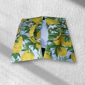 Peut inclure: Vêtement à motif de citrons sur fond bleu clair. Le vêtement présente un motif de citrons jaunes, de feuilles vertes et de fleurs blanches. Le vêtement est ouvert sur le devant et possède un col.