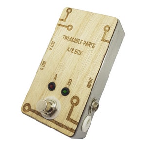 Könnte beinhalten: Eine A/B-Box aus Holz mit zwei Eingangsbuchsen, zwei Ausgangsbuchsen und einem Fußschalter. Die Box trägt ein Etikett mit der Aufschrift "Tweakable Parts A/B Box".