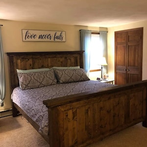May include: A rustic wooden bed frame with a headboard and footboard. The bed is made of dark-stained wood and has a patterned comforter and pillows. A sign above the bed reads "love never fails".