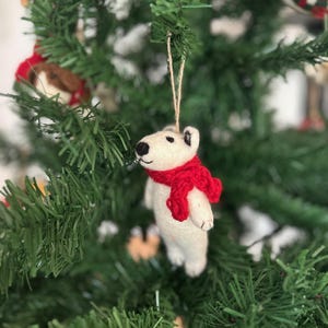 Può includere: Addobbo natalizio a forma di orso polare in feltro bianco con una sciarpa in feltro rosso appesa a un albero di Natale verde.