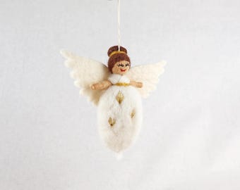 May include: A felt angel ornament featuring a brown hair bun, a white dress with gold embroidered accents, and large white wings. The figure has a stitched face with closed eyes and a red mouth, suspended by a thin white string for hanging.