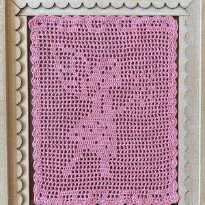 Puede incluir: Un diseño de hada de ganchillo filet rosa enmarcado en un marco de madera clara con un borde festoneado. El texto "Filet crochet fairy" está en la parte superior del marco. El ganchillo presenta una silueta de hada detallada.