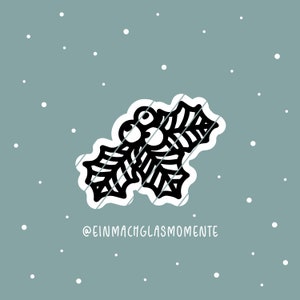 Puede incluir: Un diseño de hojas de acebo en blanco y negro con bayas rojas, sobre un fondo verde azulado apagado con acentos de copos de nieve blancos. El diseño tiene un borde blanco y es un tema festivo.