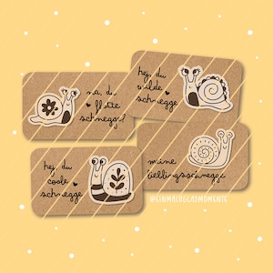May include: Four rectangular kraft paper cards featuring snail illustrations and German text. The cards display phrases like 'na, du flotte schnecke?', 'hej, du wilde schnecke', 'hej, du coole schnecke', and 'meine lieblingsschnecke' with the handle @EINMACHGLASMOMENTE.