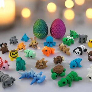 May include: A selection of brightly coloured animal erasers, including a panda, shark, and turtle, and two dragon egg-shaped erasers. The erasers are in various colours, such as blue, green, and orange, and are arranged on a light background.