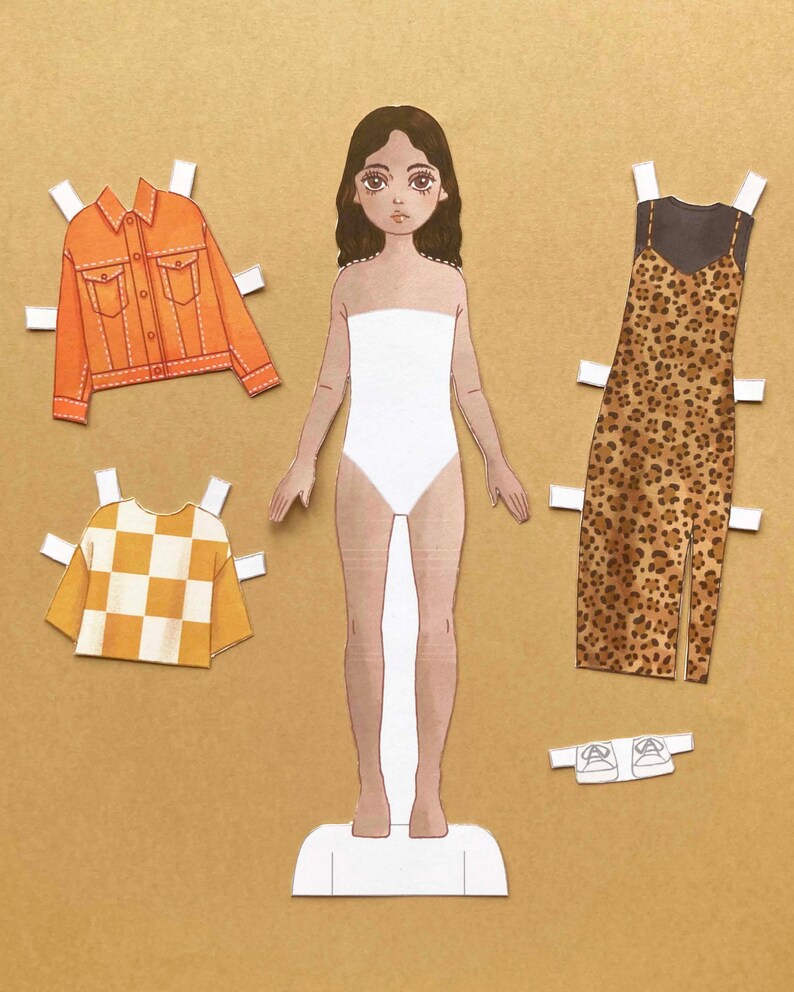 Puede incluir: Mu&ntilde;eca de papel con un vestido blanco, un vestido de estampado de leopardo marr&oacute;n y negro, una camisa a cuadros amarilla y blanca, una chaqueta vaquera y un par de zapatos blancos.