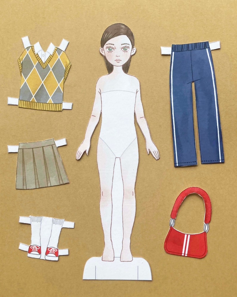 Puede incluir: Mu&ntilde;eca de papel con una variedad de opciones de ropa, incluyendo un chaleco de punto de color amarillo y marr&oacute;n, una falda plisada marr&oacute;n, un pantal&oacute;n azul con rayas blancas, un par de calcetines blancos con zapatillas rojas y un bolso de mano rojo con rayas blancas.