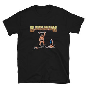Peut inclure: T-shirt noir avec une image pixelisée d'un personnage de jeu vidéo tenant une épée et le mot "BARBARIAN" en lettres brunes.