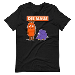 Op de afbeelding: Zwart T-shirt met een illustratie van een oranje muis en een paarse olifant. De tekst "DIE MAUS" is in oranje boven de illustratie gedrukt.