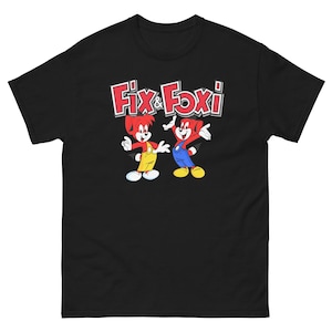 Könnte beinhalten: Schwarzes T-Shirt mit einer roten und weißen Grafik von zwei Comicfiguren, Fix & Foxi, mit dem Text "Fix & Foxi" darüber.