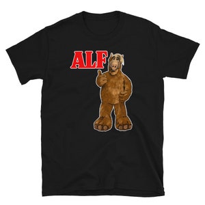 May include: Black t-shirt with a red "ALF" text and a cartoon image of ALF, a furry alien with a brown body, a long nose, and a big smile, giving a thumbs up.