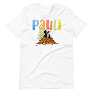 Peut inclure: T-shirt blanc avec le texte "pauli" en couleurs et un dessin animé de taupe qui sort d'un tas de terre.