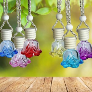 May include: Seven glass flower-shaped car air fresheners hanging from strings. The fresheners are in various colors, including blue, pink, red, purple, and yellow.