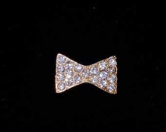 May include: A gold bow tie brooch with clear rhinestones.