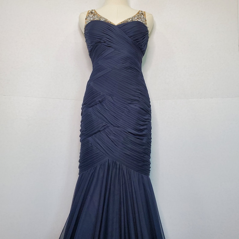 May include: A navy blue, floor-length, sleeveless gown with a sweetheart neckline and a beaded bodice.