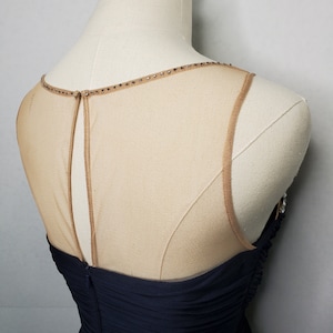 May include: A navy blue sleeveless dress with a sheer mesh panel at the back. The mesh panel is adorned with small rhinestones around the neckline.